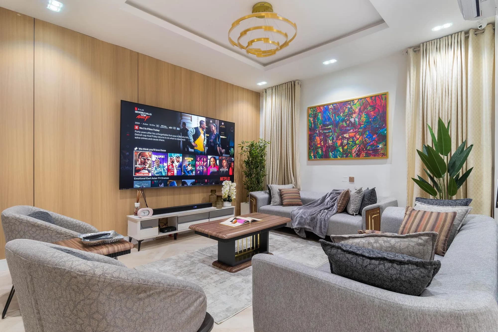 Living room with an oak-slat TV wall, gold chandelier, vivid abstract art and grey sofas