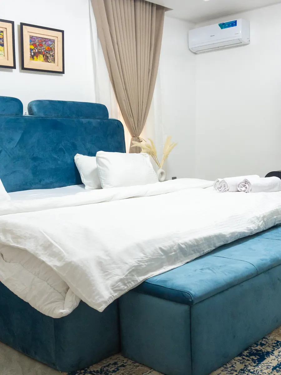 Blue velvet bedroom with a bench, wall-mounted TV and patterned rug