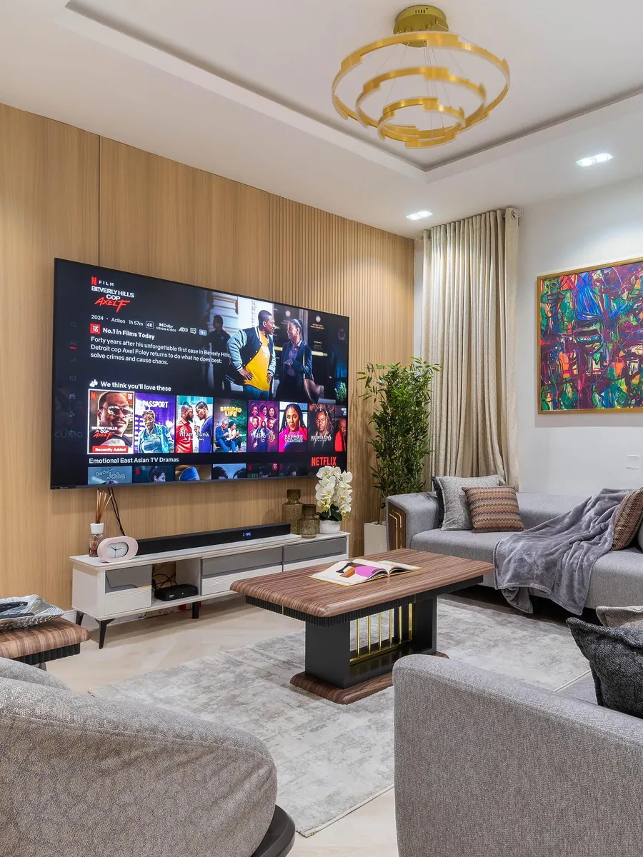 Living room with an oak-slat TV wall, gold chandelier and vivid abstract art